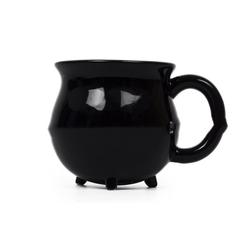 Side view of black cauldron-shaped Halloween mug showing handle and tiny cauldron feet
