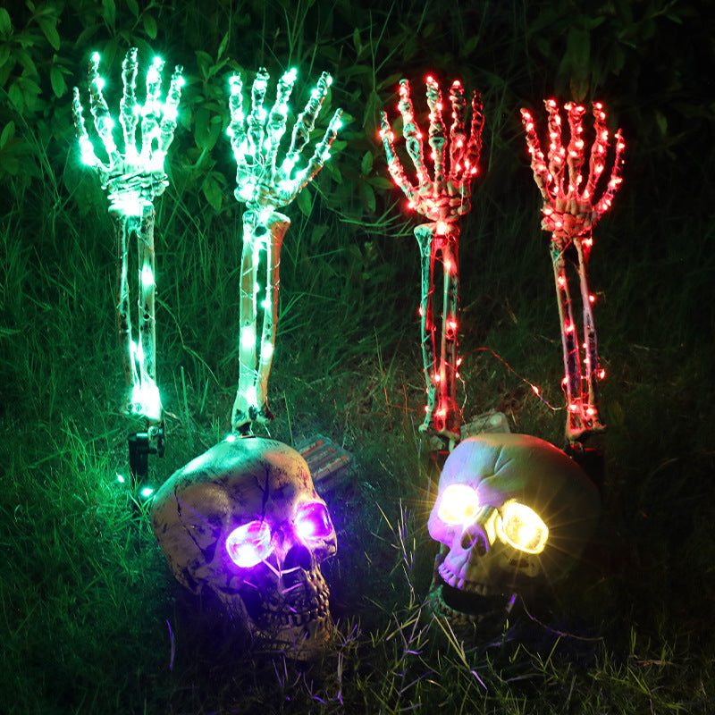 Halloween LED skeleton hand yard stakes in green and red glowing in dark grass with light-up skull decorations